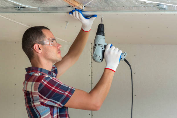 istock Young man in goggles fixing drywall suspended ceiling to metal frame using electrical screwdriver on ceiling insulated with shiny aluminum foil. Renovation, construction, do it yourself concept. 1156942531