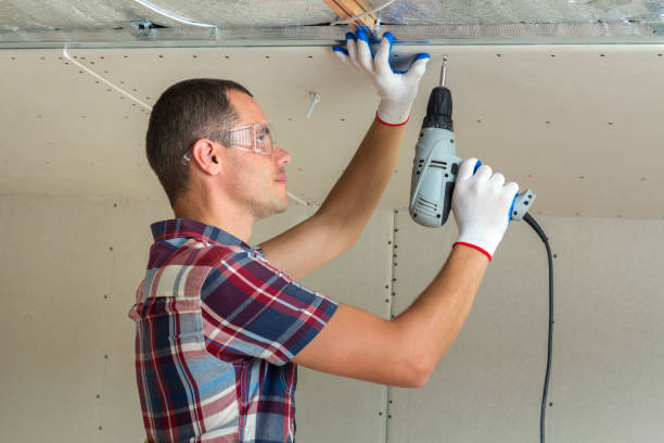 istock Young man in goggles fixing drywall suspended ceiling to metal frame using electrical screwdriver on ceiling insulated with shiny aluminum foil. Renovation, construction, do it yourself concept. 1156942532