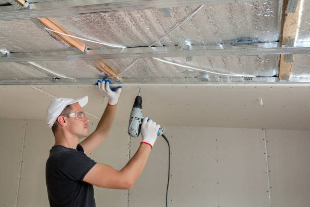 istock Young man in goggles fixing drywall suspended ceiling to metal frame using electrical screwdriver on ceiling insulated with shiny aluminum foil. Renovation, construction, do it yourself concept. 1156942540