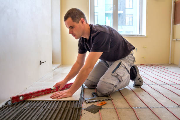 istock Young worker tiler installing ceramic tiles using lever on cement floor with heating red electrical cable wire system. Home improvement, renovation and construction, comfortable warm home concept. 1156942556