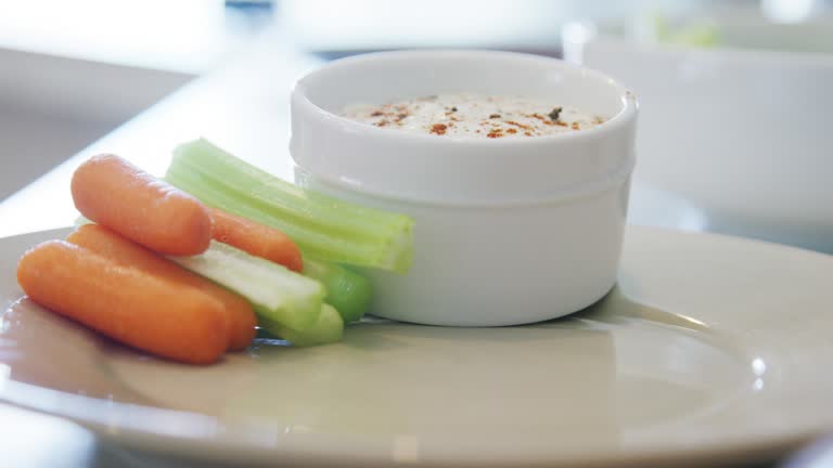 A Caucasian Person's Hand Stacks Carrot and Celery Sticks Neatly on a Plate Next to a Small Bowl of Ranch Dipping Sauce