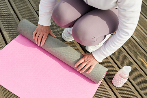 High angle close up of contemporary woman unrolling pink yoga mat on wooden pier outdoors, copy space