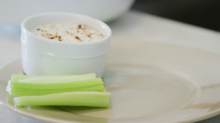 A Caucasian Man's Hand Places Celery Sticks Neatly on a Plate Next to a Small Bowl of Ranch Dipping Sauce