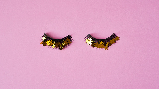 Studio shot of a pair of false eyelashes with golden stars on them against a pink background