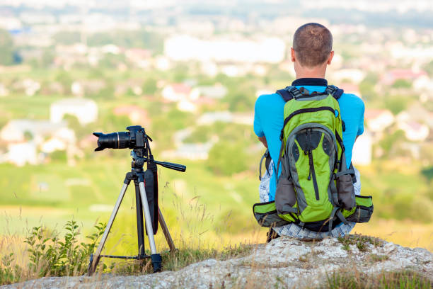 istock Hiker photographer  sitting on a rock looking forward near a camera on a tripod 1156948667