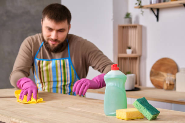 istock Young handsome bearded man in the kitchen, trying to clean a table using detergents, brushes, sprays 1156950546