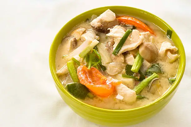 Tom Kha Gai, a traditional dish from Thailand served in a bright green ceramic bowl and set against a white background