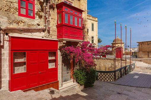 The traditional Maltese street with red phone box and building with colorful shutters and balconies at sunrise, Valletta, Capital city of Malta