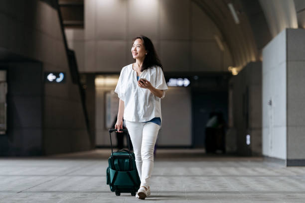 Chinese woman in station with wheeled suitcase Smiling senior woman arriving in airport and using mobile phone, technology, travel, on the go taiwan people stock pictures, royalty-free photos & images