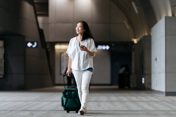 chinese woman in station with wheeled suitcase - business travel people traveling airport journey imagens e fotografias de stock