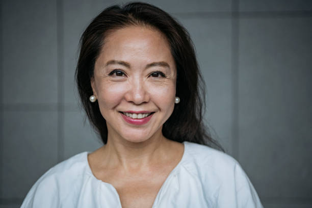 Attractive senior Chinese woman smiling Headshot of businesswoman in her 60s looking at camera, confidence, cheerful, beauty chinese ethnicity stock pictures, royalty-free photos & images