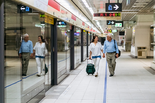 Chinese man and woman in their 60s with luggage, walking and looking at each other, travel, togetherness, on the move