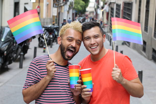 pares gays étnicos que comemoram a diversidade ao ar livre - flag gay man american culture rainbow - fotografias e filmes do acervo