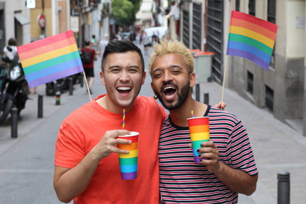 pares gays étnicos que comemoram a diversidade ao ar livre - flag gay man american culture rainbow - fotografias e filmes do acervo