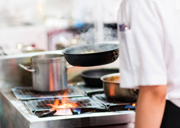 istock Chef cooking with flame in a frying pan on a kitchen stove 1156965048
