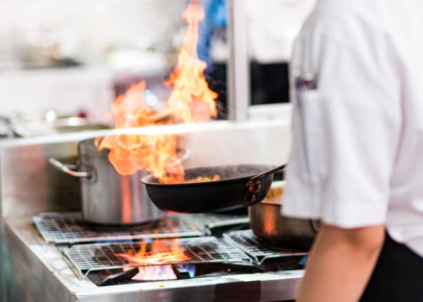 Close-up of chef cooking something delicious on stove, burning flame from dish. Impressive show for visitors on open air. Cooking, cafe, takeaway concept