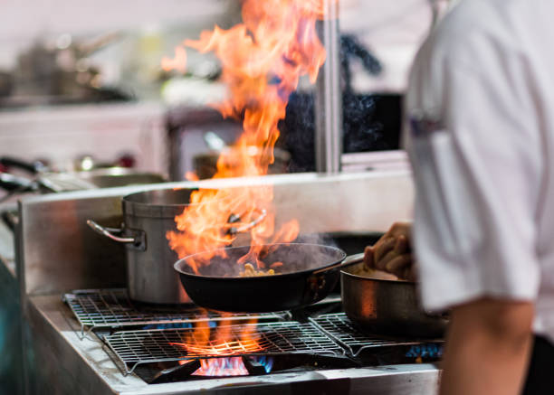 istock Chef cooking with flame in a frying pan on a kitchen stove 1156965057