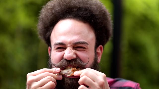Bearded hipster with a pointy mustache eating a chicken wing