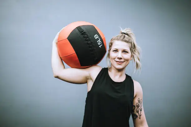 A portrait of smiling physical trainer getting ready to lead a class in her gym.  She holds a medicine ball for their next routine.