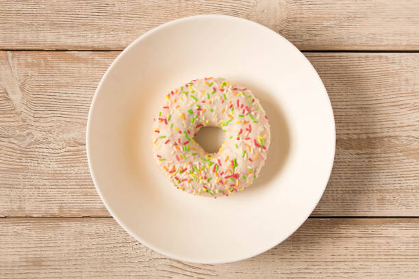 istock Fresh glazed donut with colorful sprinkles on a white plate. 1156975685