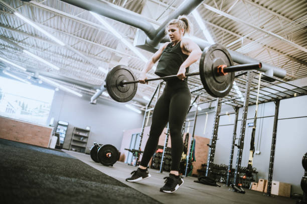 Female Trainer At Cross Training Gym A physical trainer performs clean and jerk olympic lifts with a barbell in preparation for a class in her small gym. clean and jerk stock pictures, royalty-free photos & images