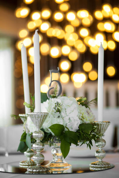istock Wedding table setting is decorated with fresh flowers and white candles. Wedding floristry. Bouquet with roses, hydrangea and eustoma. On the background blur are burning garlands with light bulbs 1156979433