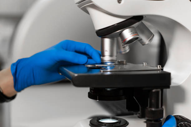 istock man in blue gloves install glass with material for research into microscope. 1156985078