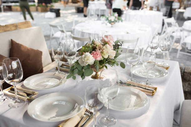 istock Wedding table setting decorated with fresh flowers in a brass vase. Wedding floristry. Banquet table for guests outdoors with a view of green nature. Bouquet with roses, eustoma and eucalyptus leaves. 1156986429