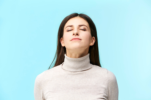 portrait of a beautiful young caucasian woman, eyes closed, smelling fragrance in the air, isolated on blue background