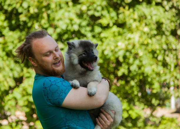 istock Young man and keeshond puppy 1156987515