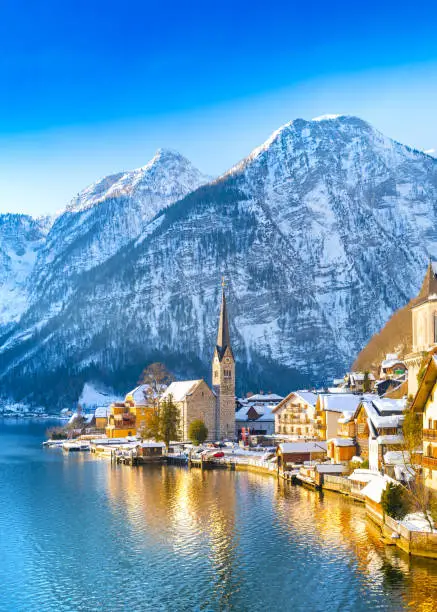 Classic postcard view of famous Hallstatt lakeside town in the Alps with traditional passenger ship on a beautiful cold sunny day with blue sky and clouds in winter, Austria