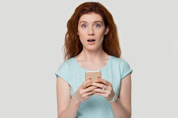 istock Surprised redhead woman shocked by text message on cell 1157002188