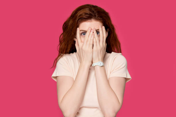 istock Scared redhead girl cover face peeking through fingers 1157002259