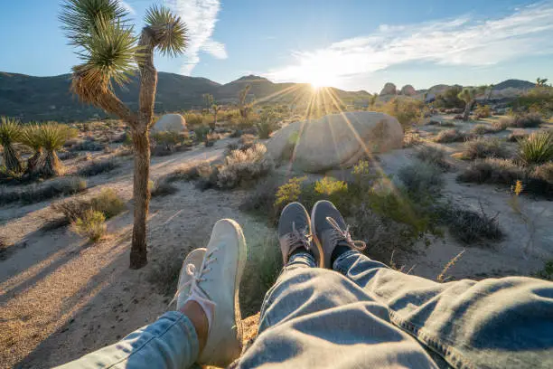 Personal perspective of couple relaxing on top of boulder rock at sunrise; feet view; 
People travel vacations relaxation concept