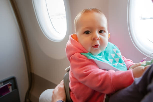 Mother and baby sitting together in airplane. First flight of infant girl. She is amazed stock photo