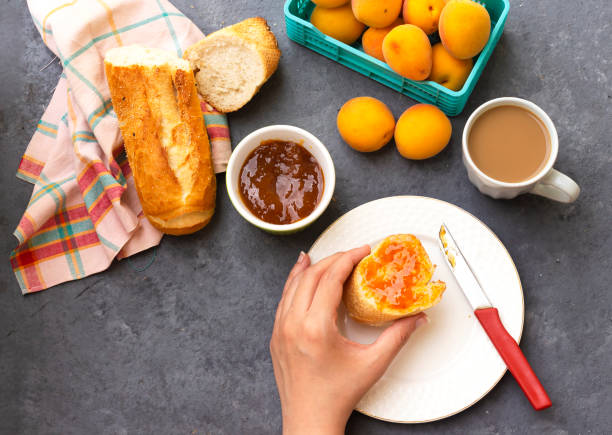 closeup woman hand is eating apricot jam slice bread with milk cup