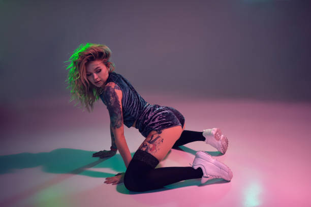 beautiful caucasian blonde girl in velour blue booty shorts and black stockings dancing twerk on her knees on pink background stock photo