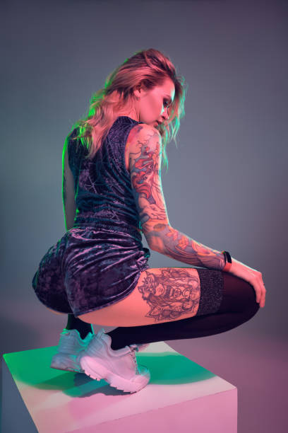 młoda blondynka fitness ubrana w niebieskie welurowe szorty z łupem pozujące przed kamerą, robiąc przysiady na szczycie dużej kostki - tattoo women sensuality back zdjęcia i obrazy z banku zdjęć