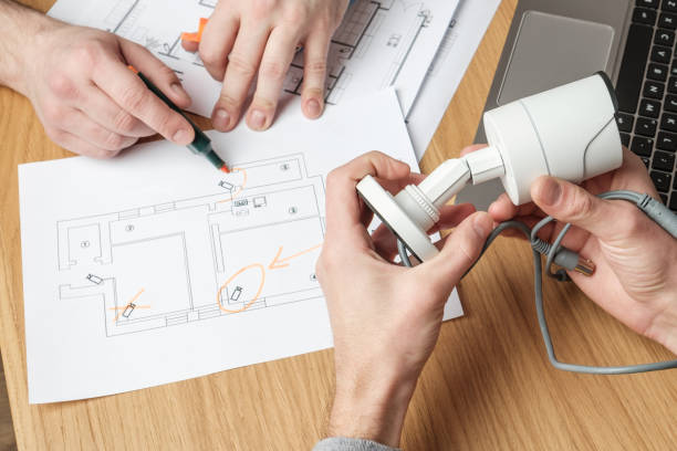 istock Two people discussing CCTV project. Video security equipment and blueprint on a table 1157010374