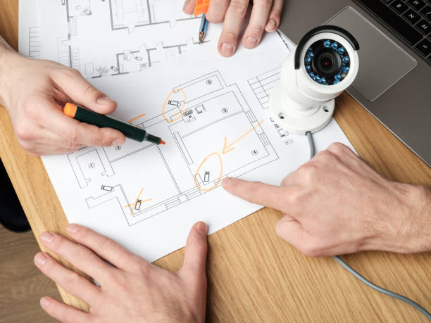 istock Two people discussing CCTV project. Video security equipment and blueprint on a table 1157010376
