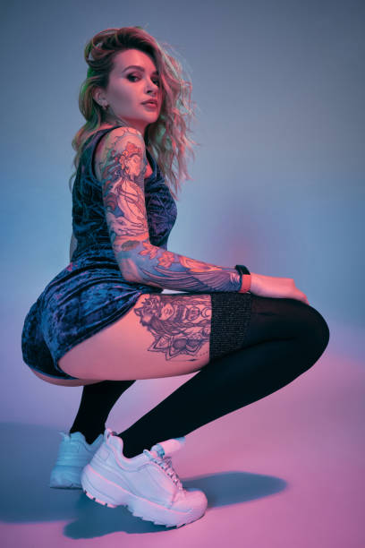 Young fitness blonde woman wearing blue velour booty shorts posing on camera, making squats in studio stock photo