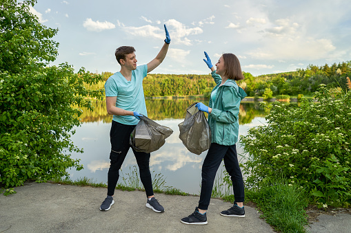 Friends crouching with bag picking up trash doing plogging.Plogging concept. Boy and girl picking up trash from the forest. They collecting the litter in garbage bag