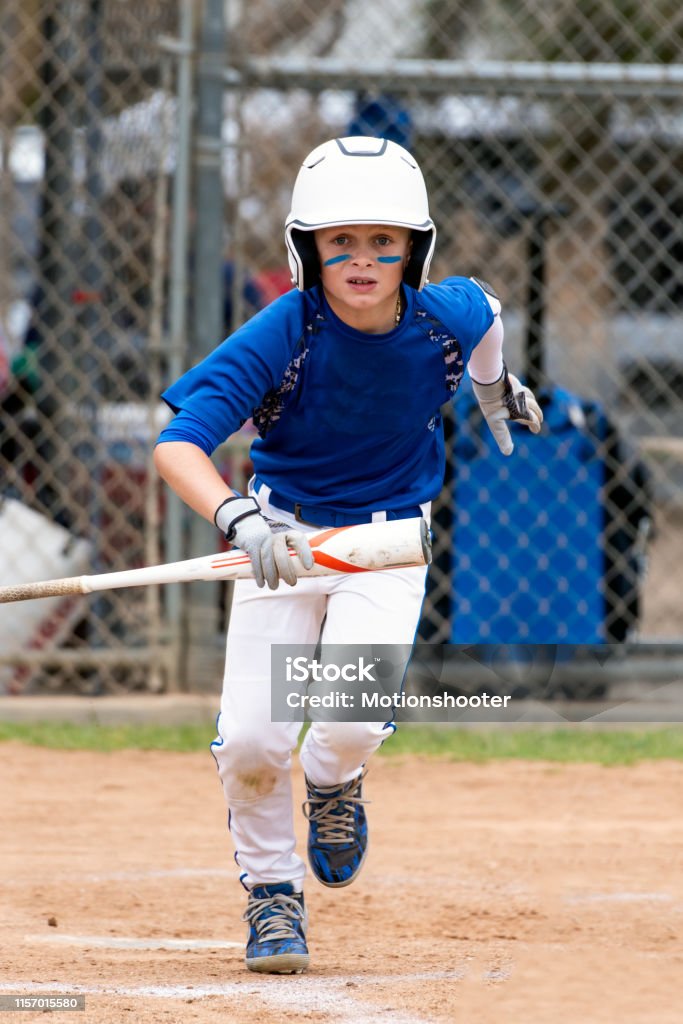 Baseball player leaving it all out on the field. Youth baseball player in blue uniform and white helmet running up the base line with bat in hand. Baseball - Sport Stock Photo