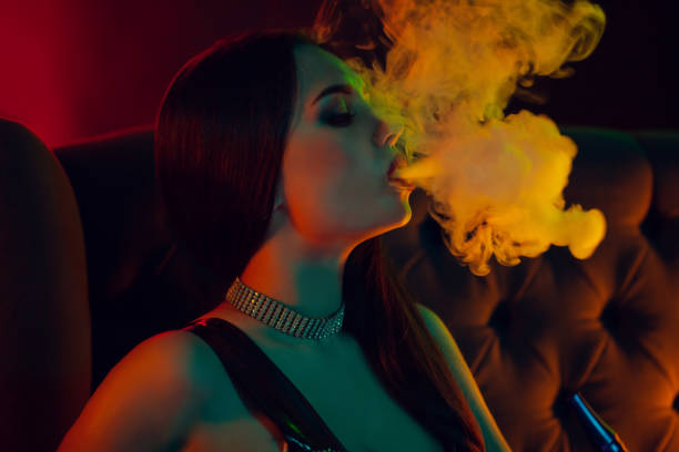 Beautiful brunette model is smoking a hookah exhaling a smoke at a luxury night club stock photo