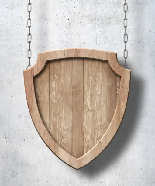 Wooden defense protection shield shaped sign made of bright natural wood and hanging on chains with concrete wall background