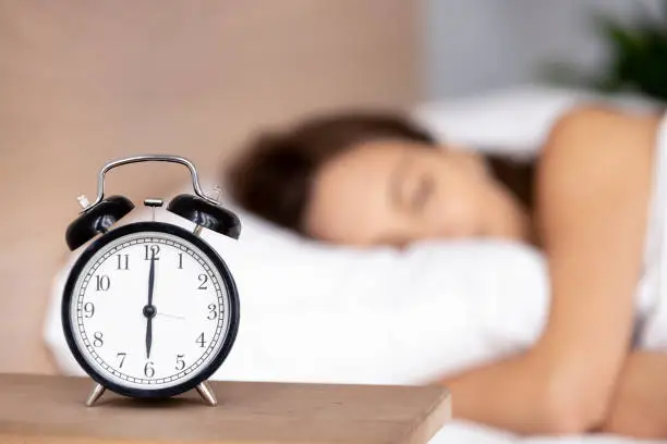 Photo of Alarm clock on bedside table with woman sleeping on background