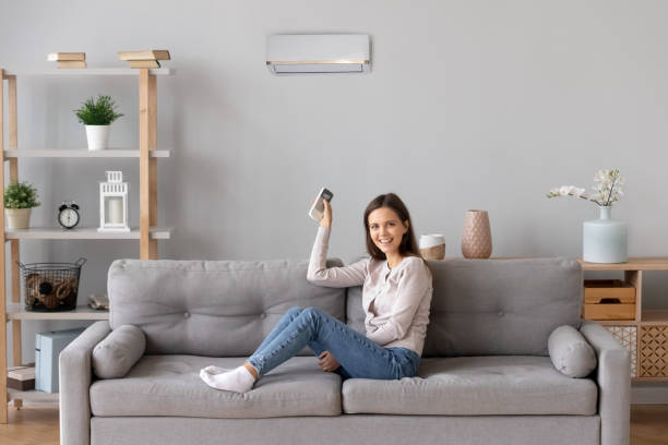 istock Smiling girl relax on couch turn on air conditioner 1157025866