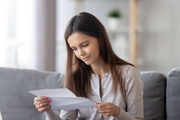 Young woman sit on couch reading paper letter Smiling young woman sit on couch reading paper letter get to know good pleasant news, happy girl on sofa receive message from bank consider examine paperwork at home checking statements college acceptance letter stock pictures, royalty-free photos & images