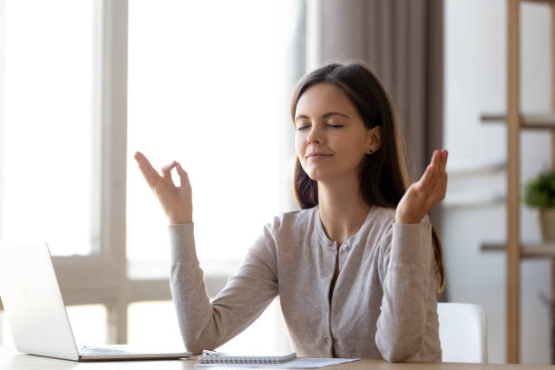 Peaceful young woman practice yoga sitting at home desk Peaceful young woman sit at table working at laptop take break meditating relieving negativity, calm girl student or millennial female distracted practice yoga at home desk. Stress free concept Distracted stock pictures, royalty-free photos & images