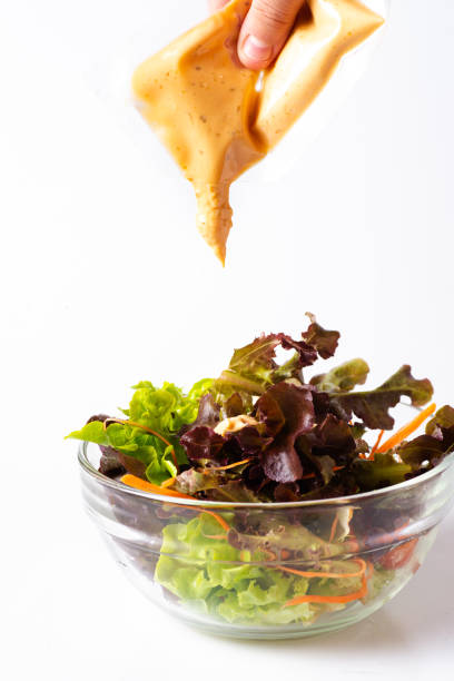 istock Hand pouring thousand island dressing on salad bowl, isolated on white. 1157038446